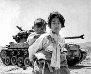 Med sin lillebror på ryggen passerar en koreansk flicka på flykt framför en M-26 Pershingstridsvagn, Haengju 1951